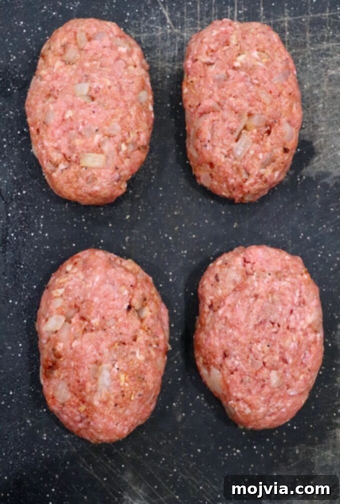 Four perfectly formed oval beef patties, approximately one inch thick, resting on a cutting board, ready for searing.