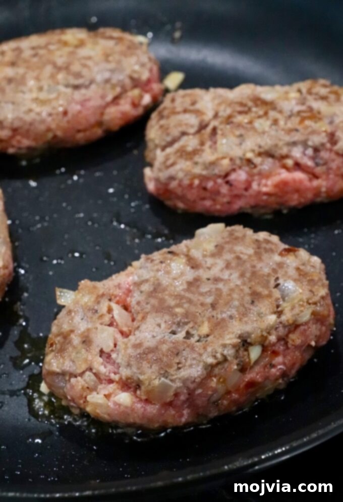 Beef patties being seared to a beautiful golden brown in a hot skillet, creating a delicious crust.