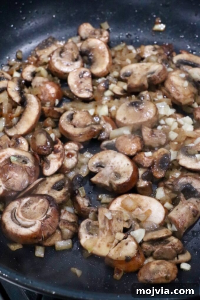 Sliced mushrooms cooking in a large skillet, beginning to soften and release their moisture.