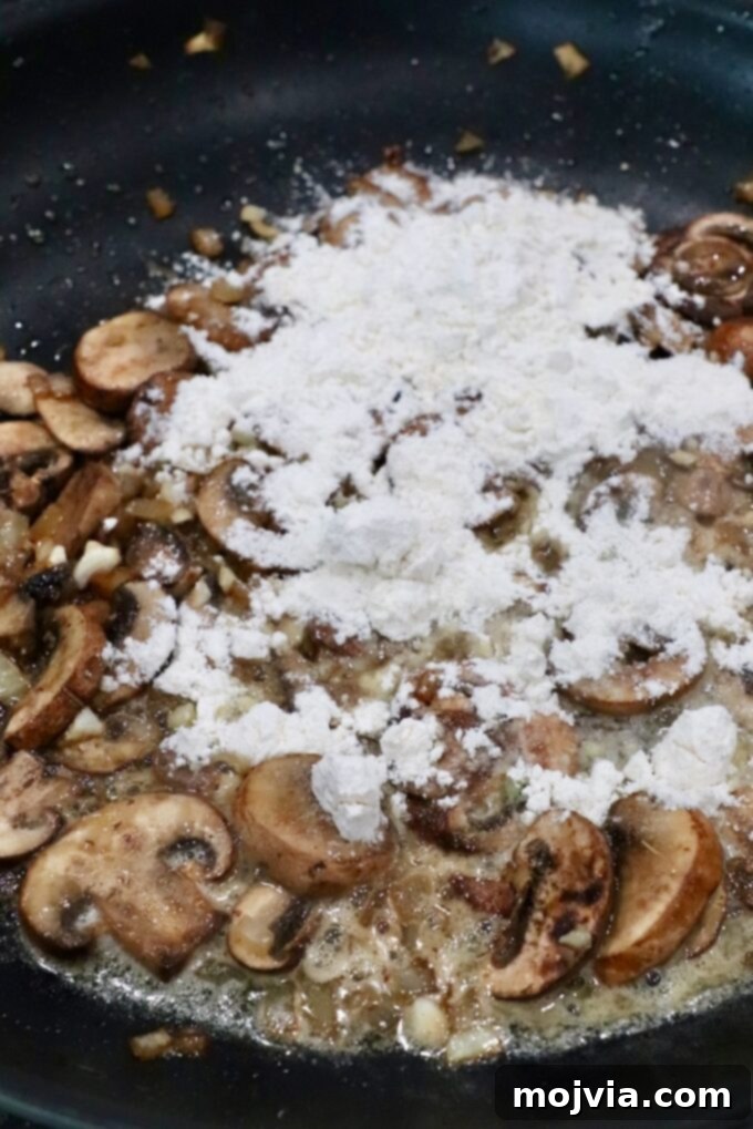Mushrooms and other aromatics in a skillet lightly dusted with flour, forming the base of a rich roux for the gravy.