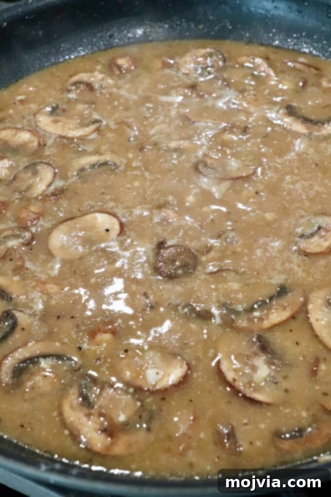 Smooth, bubbling mushroom gravy simmering in a skillet, thick and ready for the Salisbury steaks.
