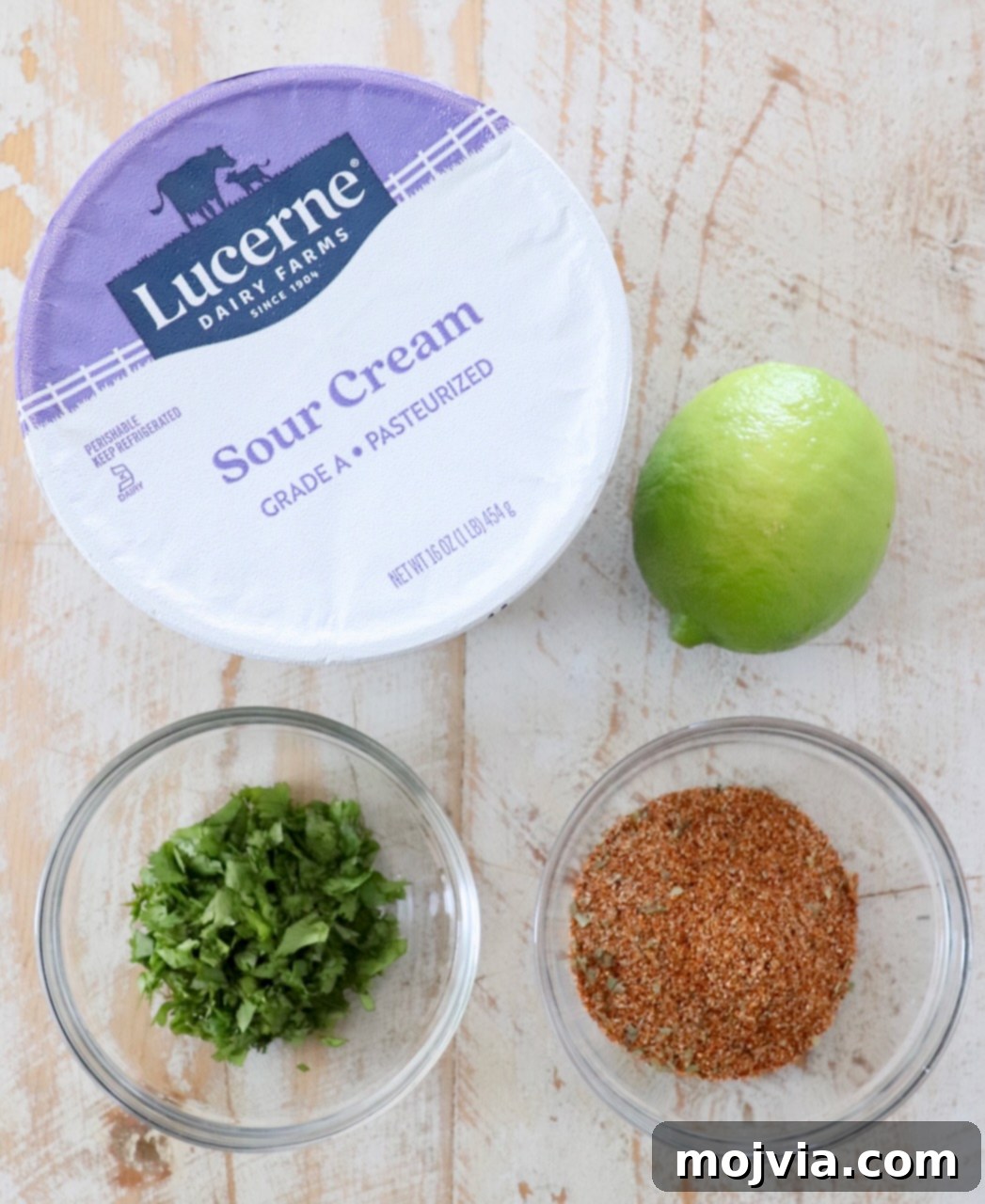 All four ingredients for homemade Southwest Salad Dressing laid out on a white wooden board: sour cream, lime, cilantro, and southwest seasoning.