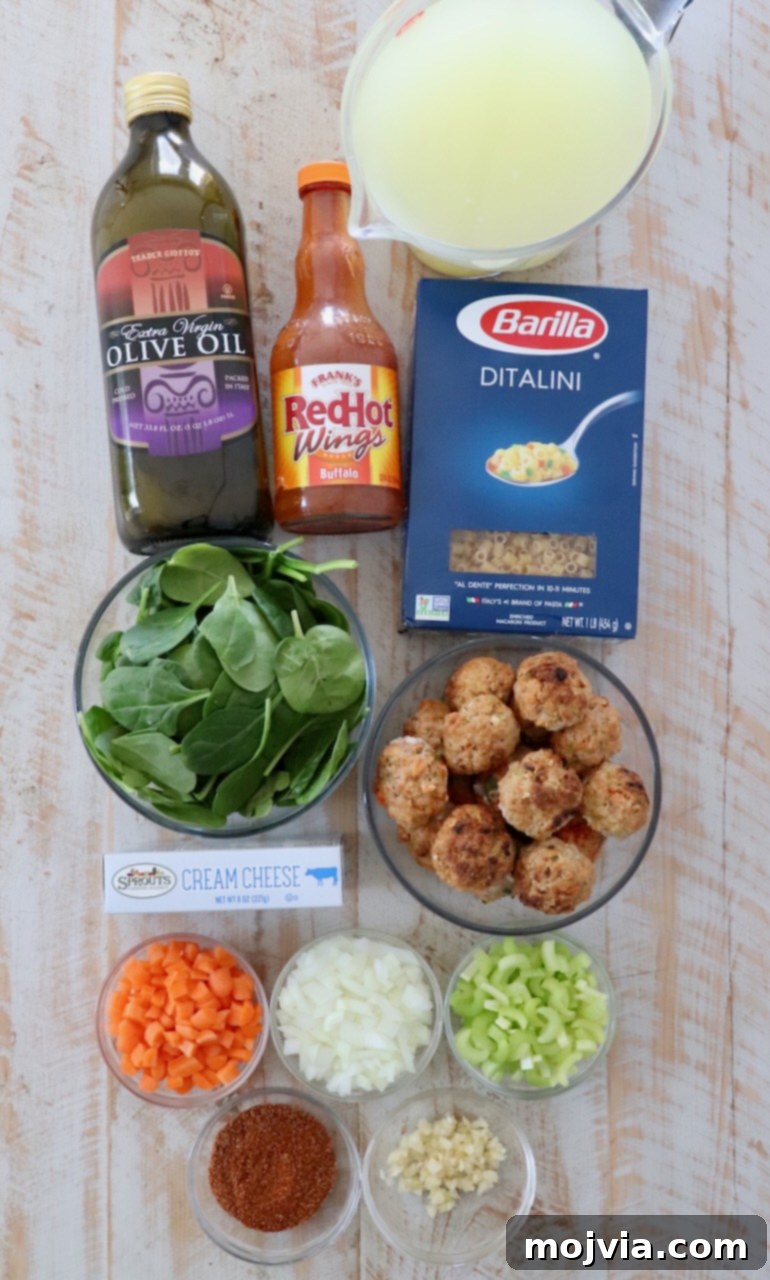 Bold Buffalo Chicken Soup 3 Fresh ingredients laid out on a white wooden board for making buffalo chicken meatball soup: carrots, celery, onions, garlic, buffalo sauce, chicken broth, pasta, spinach, and cream cheese.