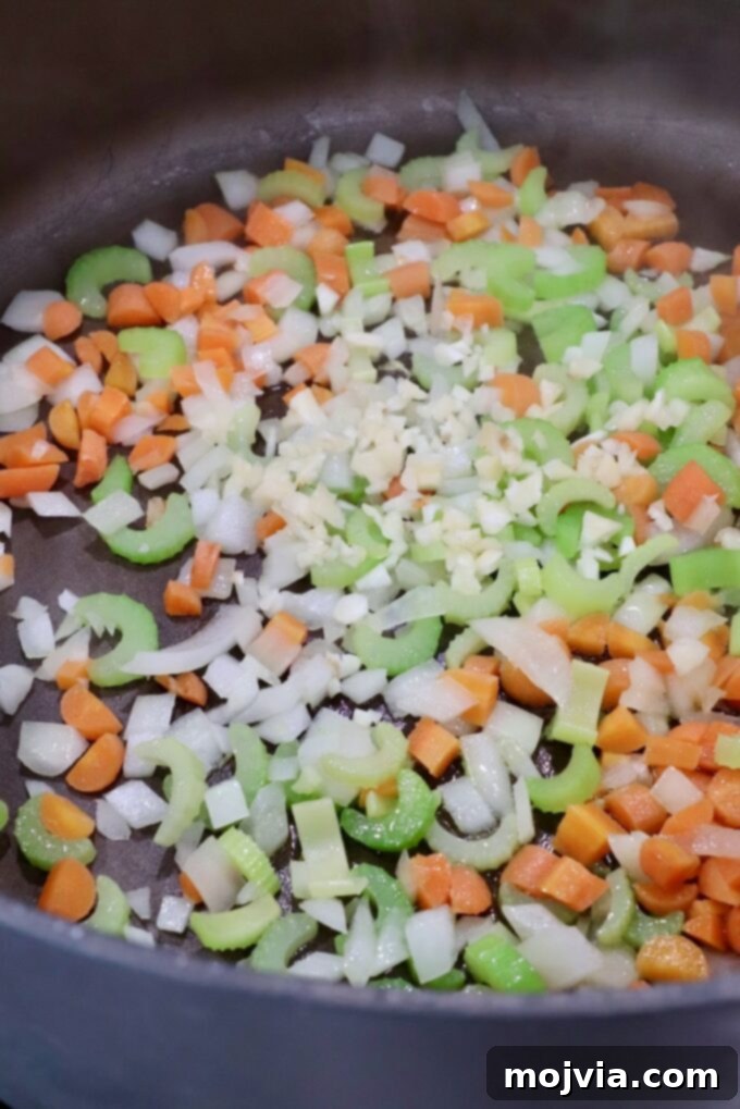 Bold Buffalo Chicken Soup 4 Diced onions, carrots, celery, and minced garlic simmering in olive oil in a large pot, forming the aromatic base for the soup.