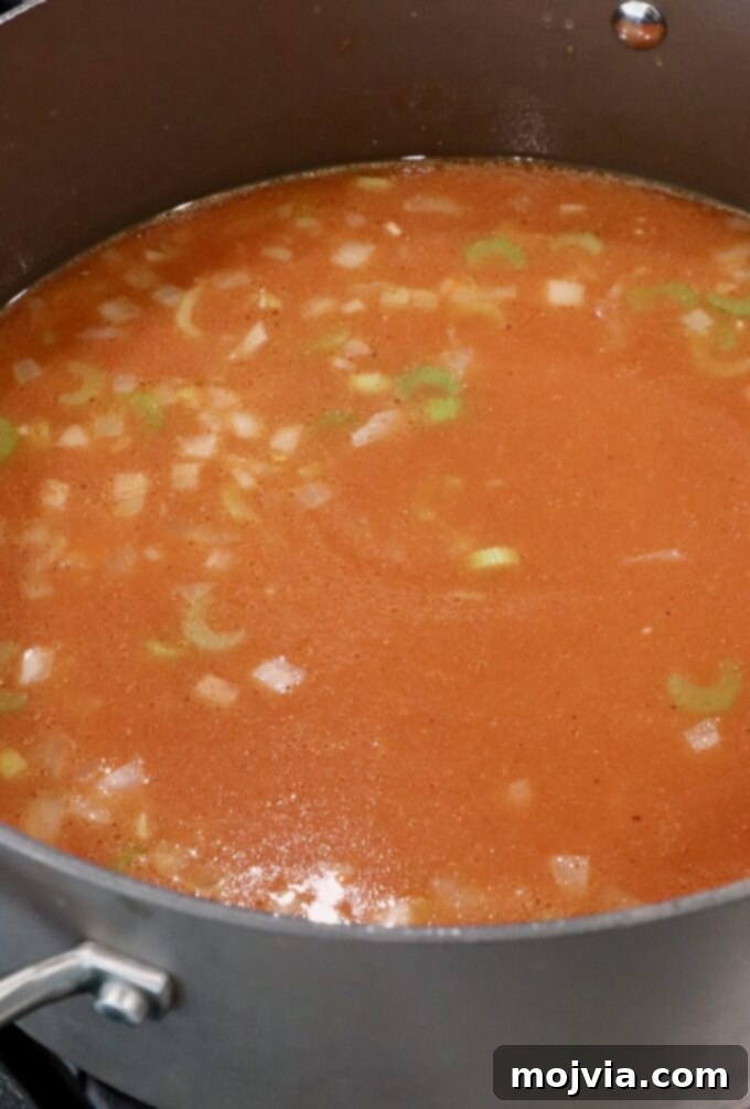 Bold Buffalo Chicken Soup 5 Chicken broth seasoned with buffalo sauce and chicken wing seasoning, mixed with diced vegetables, simmering in a pot.