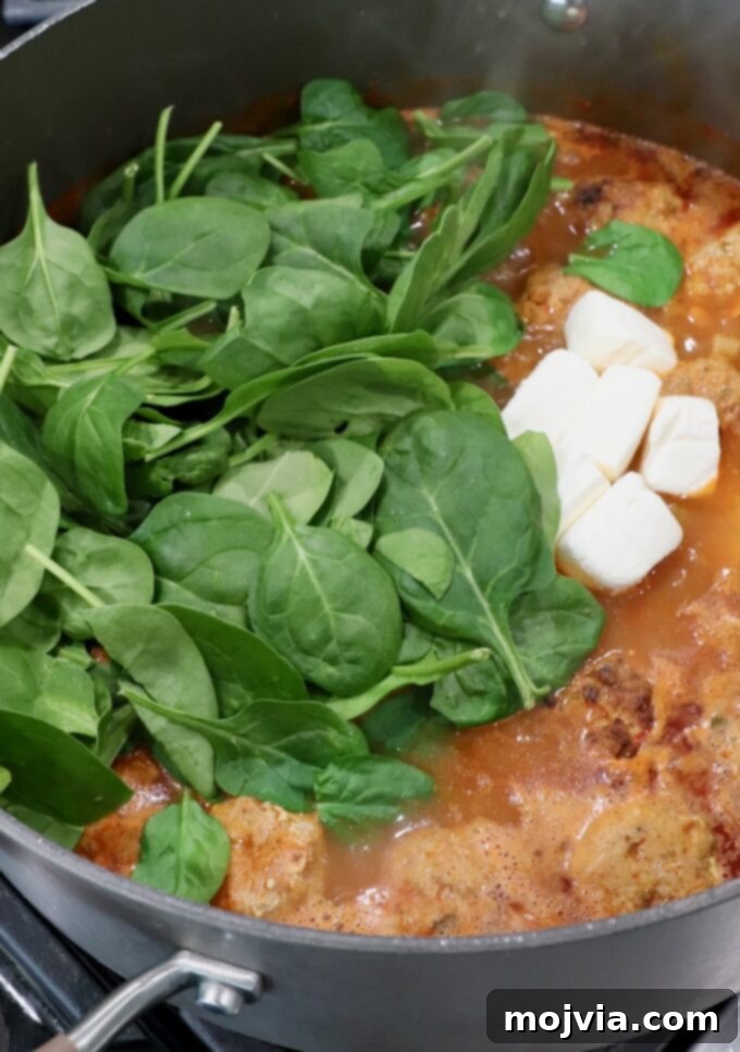 Bold Buffalo Chicken Soup 7 Fresh spinach leaves and cubes of softened cream cheese being stirred into the hot buffalo chicken meatball soup, ready to melt and create a creamy texture.