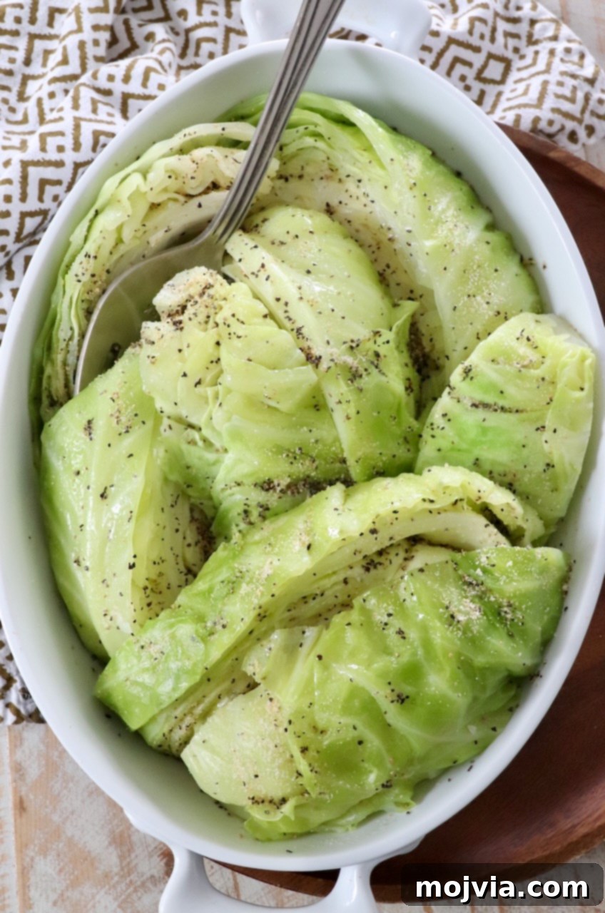 A serving dish filled with perfectly steamed cabbage, ready to be enjoyed with a serving fork resting beside it. The cabbage glistens lightly, showing its vibrant green color.