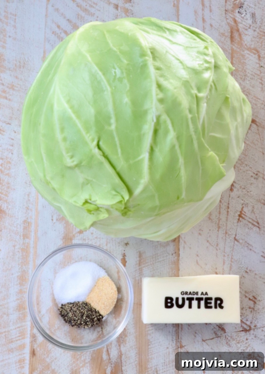 Ingredients for simple steamed cabbage laid out on a white wooden board, including a fresh green cabbage, a stick of butter, salt, black pepper, and garlic powder.