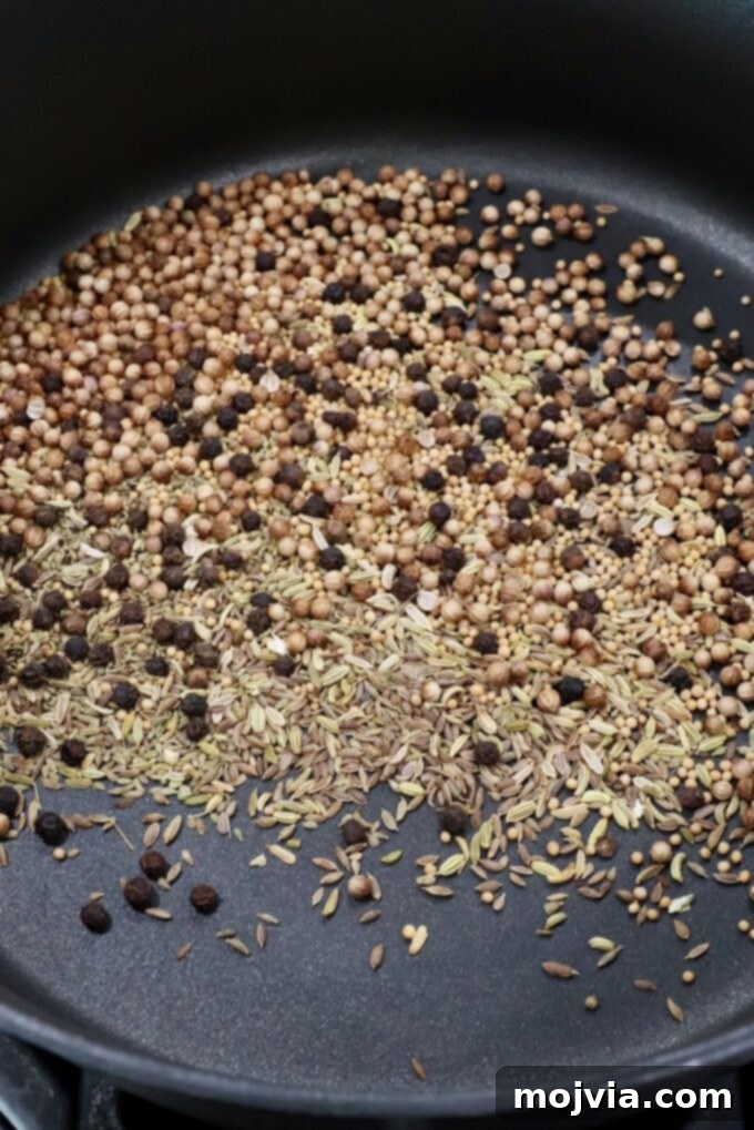 Signature Corned Beef Spice Blend 4 An assortment of whole spices, including coriander, mustard, peppercorns, anise, fennel, dill seeds, and whole cloves, lightly toasting in a skillet on the stove to release their fragrant aromas.