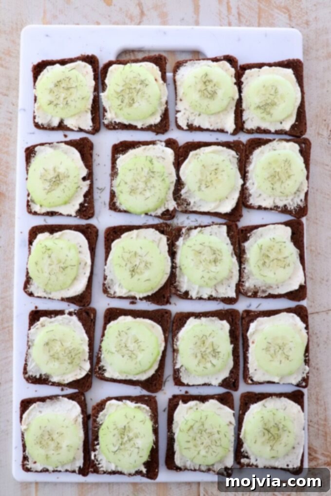 Delicate Cucumber Delights 7 Finished cucumber sandwiches with dill sprinkled on top, on a cutting board.