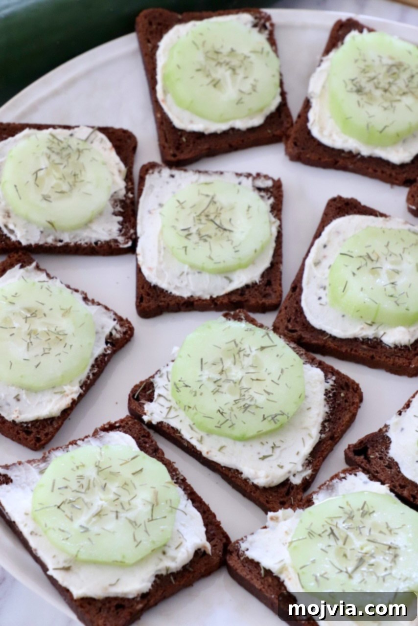 Delicate Cucumber Delights 9 Open-faced cucumber tea sandwiches with dill on a white plate, ready to be served.