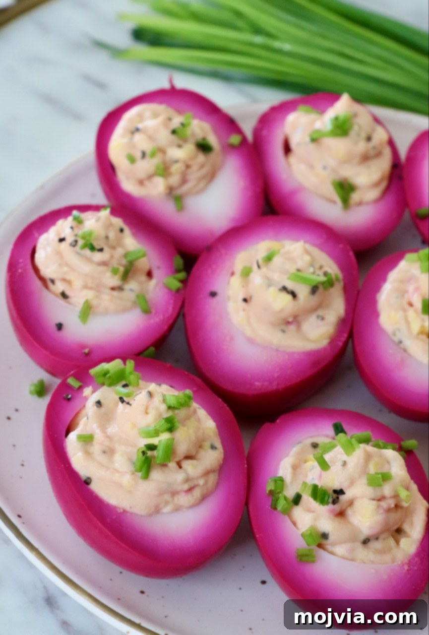 Beet pickled deviled eggs elegantly arranged on a plate, garnished with fresh chives.