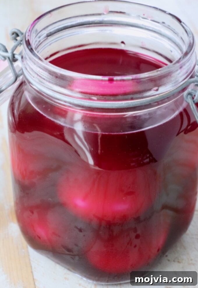 Hard-boiled eggs submerged in vibrant red pickled beet juice inside a glass jar.