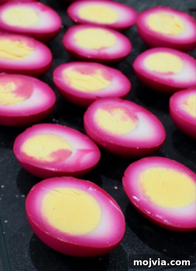 Beet-pickled hard-boiled eggs, now bright pink, neatly sliced in half on a cutting board.