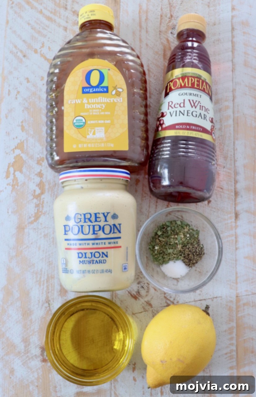 A collection of fresh ingredients for Italian dressing, including lemons, red wine vinegar, olive oil, and herbs, arranged on a rustic white wooden board.