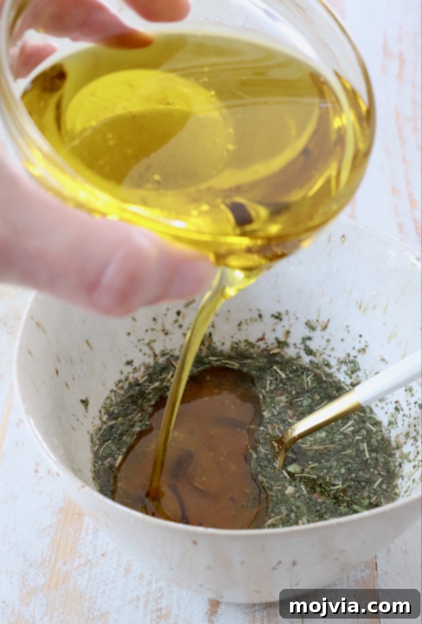 Olive oil being poured into a mixing bowl already containing red wine vinegar and Italian herbs, illustrating the emulsification process for Italian dressing.