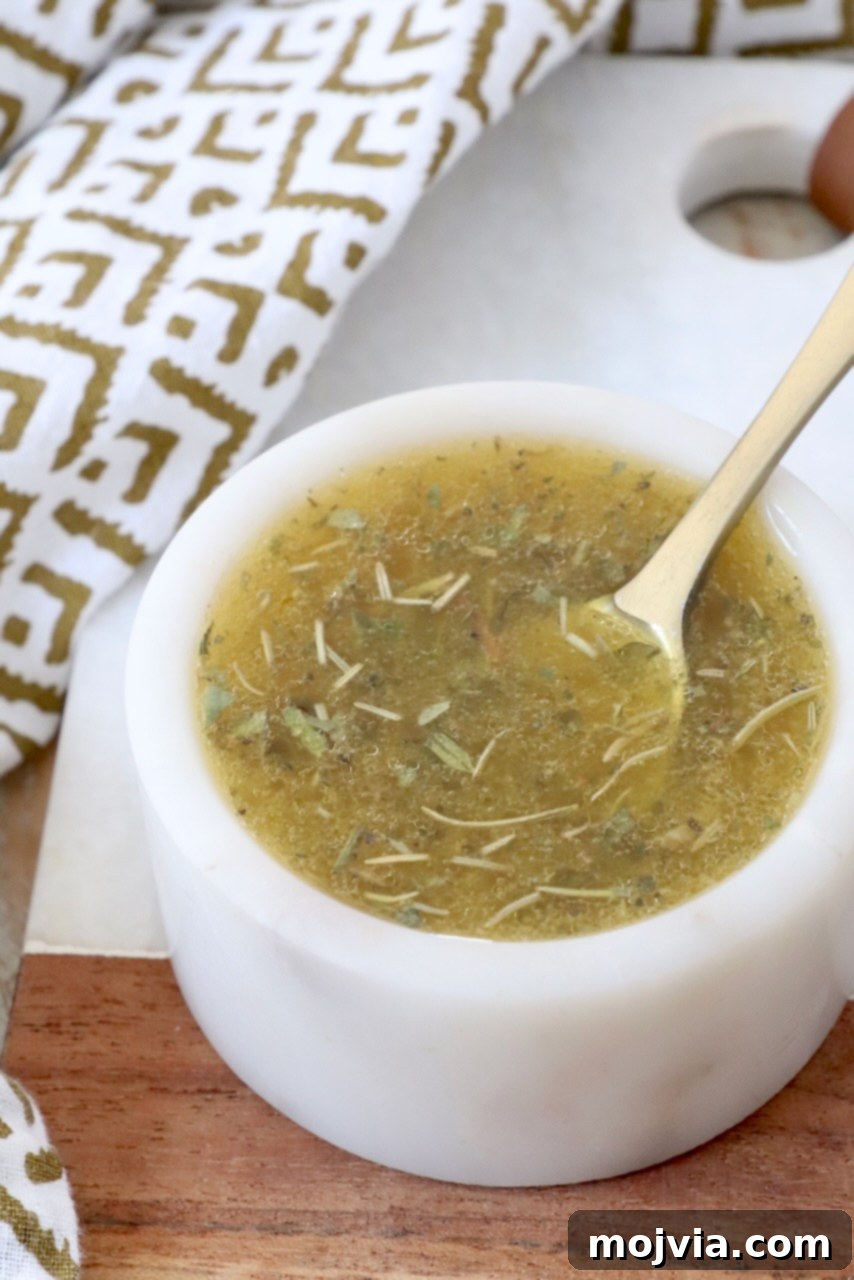 A small glass bowl filled with homemade Italian dressing, garnished with fresh herbs and a spoon, emphasizing its rich texture and readiness for use.