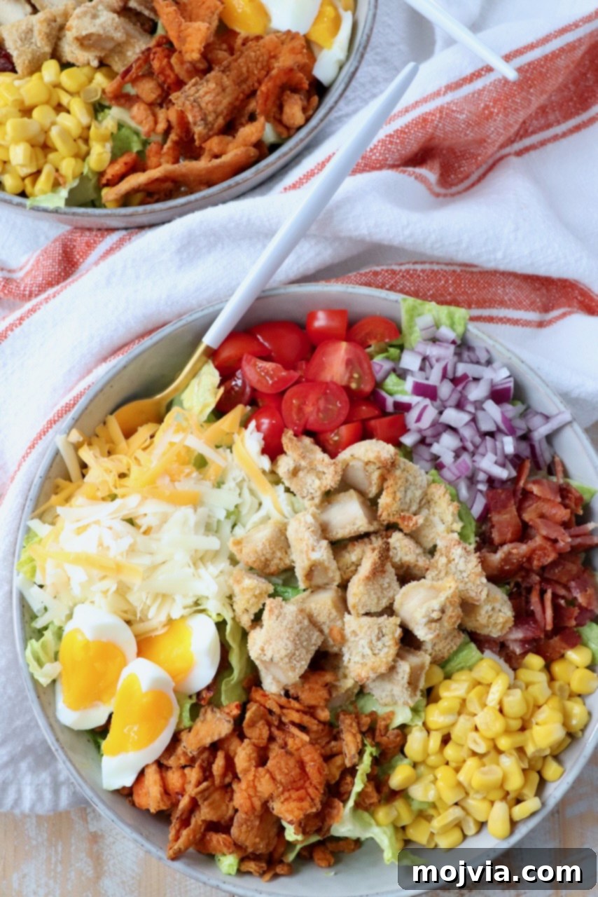 A vibrant Crispy Chicken Salad in a bowl, featuring golden chicken strips, fresh greens, corn, tomatoes, and bacon, ready to be enjoyed with a fork.