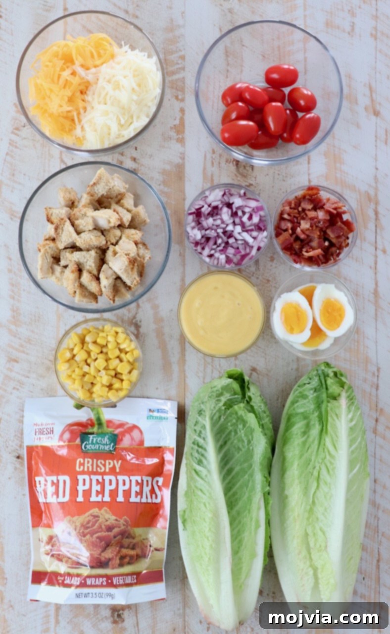Fresh ingredients for Crispy Chicken Salad laid out on a white wooden board, including romaine lettuce, corn, tomatoes, bacon, cheese, and eggs.