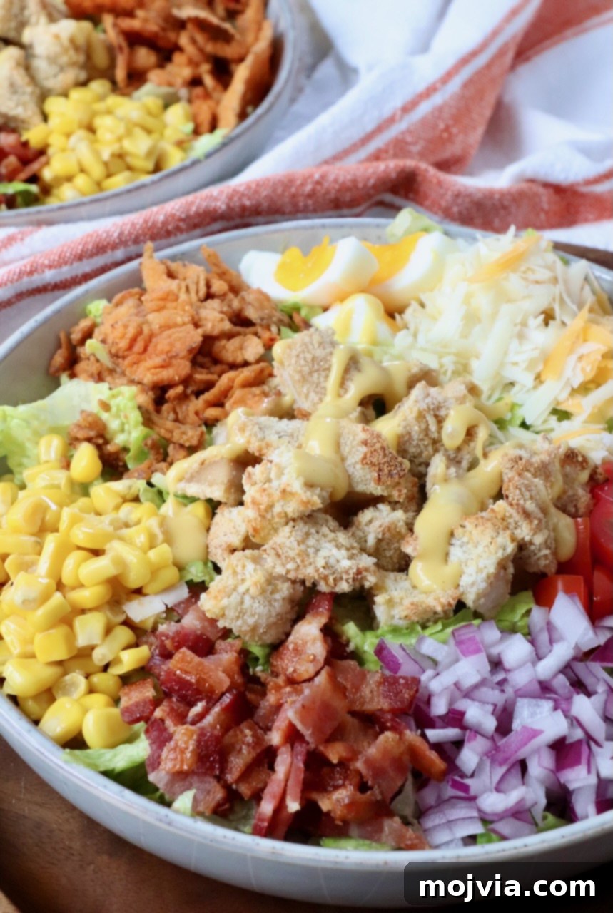 A close-up shot of a single bowl of Crispy Chicken Salad, showcasing the golden chicken, colorful vegetables, cheese, and bacon.