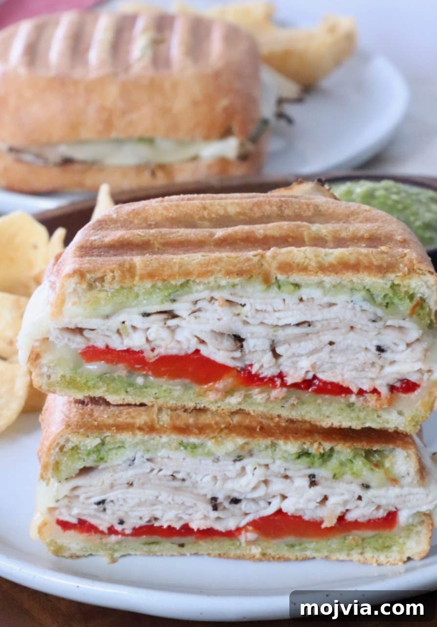 Herbed Turkey Pesto Stack 2 A delicious turkey pesto sandwich, sliced in half and stacked on a plate, showcasing its golden-brown ciabatta, melted provolone, and vibrant pesto.