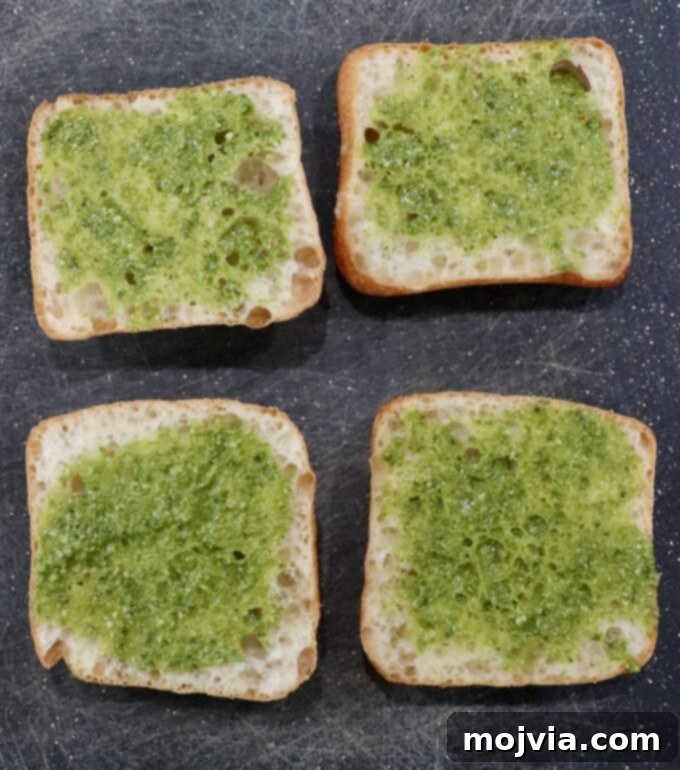 Herbed Turkey Pesto Stack 4 Spreading vibrant basil pesto generously onto the cut sides of ciabatta rolls, preparing the foundation for a flavorful sandwich.