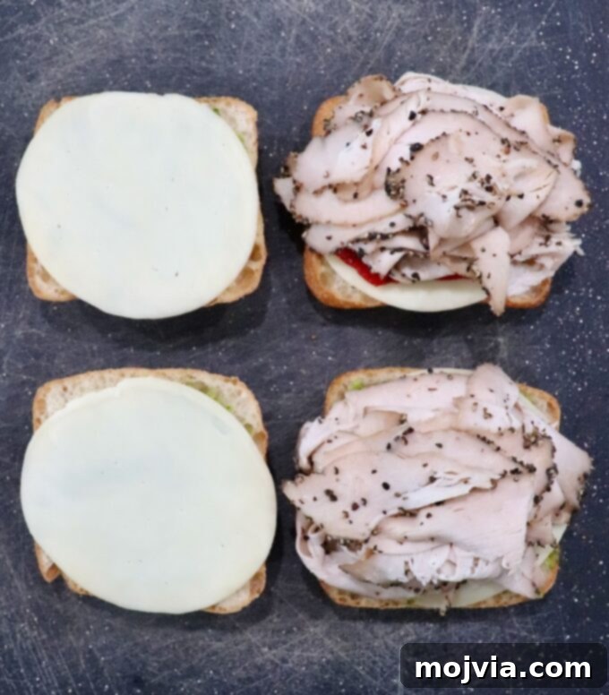 Herbed Turkey Pesto Stack 6 Layers of thinly sliced turkey artfully arranged over the provolone cheese and roasted red peppers on ciabatta rolls, ready for the top bread layer.