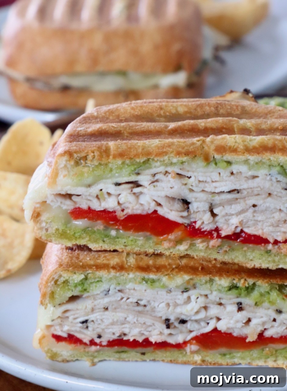 Herbed Turkey Pesto Stack 9 A perfectly golden-brown turkey panini, sliced diagonally and stacked on a white plate, highlighting the melted cheese and delicious fillings.
