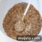 A bowl of vibrant homemade lemon pepper seasoning, accompanied by a small spoon, highlighting its texture and fresh appeal.