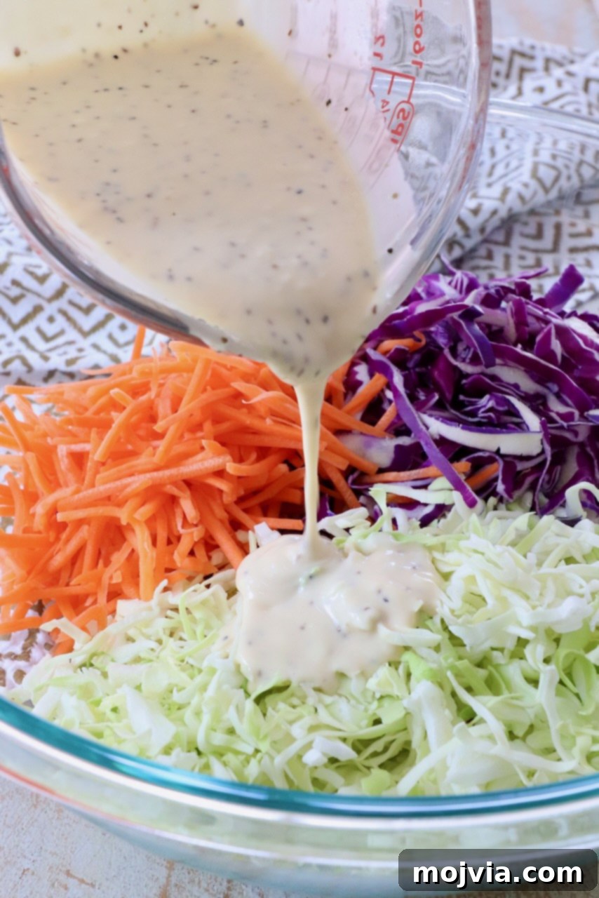 Zesty Coleslaw Dressing 6 Homemade coleslaw dressing being poured from a glass measuring cup over shredded cabbage in a large glass bowl