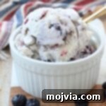 scoops of blueberry ice cream in small bowl with gold spoon