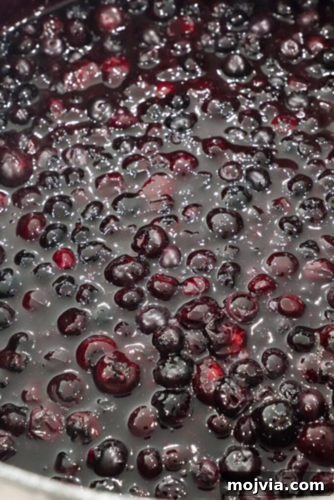 Frosted Blueberry Dream 5 Blueberry pie filling simmering and thickening in a large saucepan, showing its rich, dark color and bubbly texture.