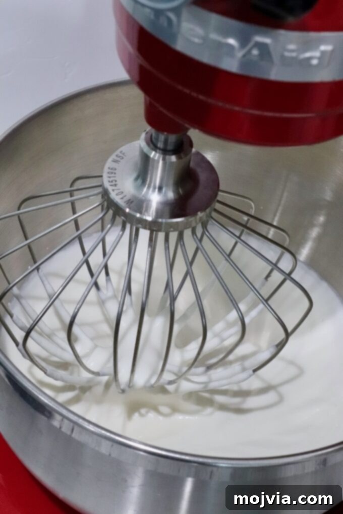 Frosted Blueberry Dream 7 Heavy cream being whipped in a stand mixer with a whisk attachment, showing the cream beginning to thicken and form peaks.