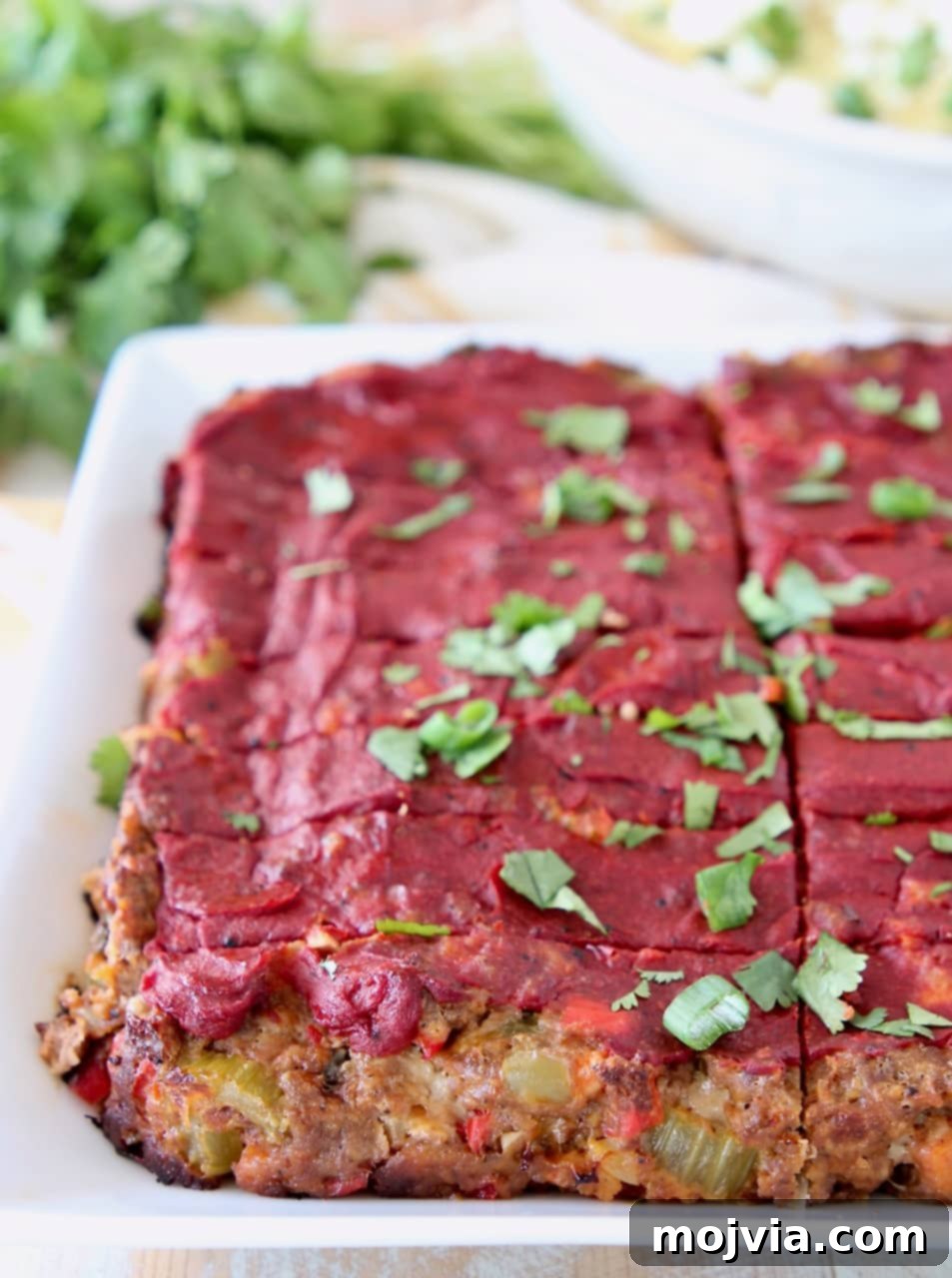 Mexican meatloaf topped with tomato paste, sliced on a white plate with fresh cilantro