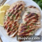 sliced grilled chicken on plate with lemon wedges