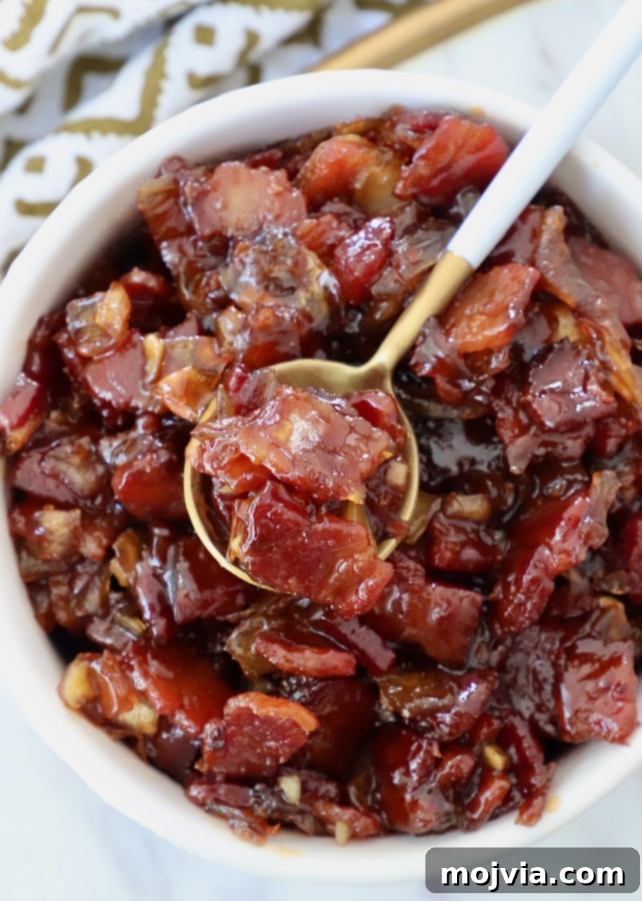 Sweet & Savory Bacon Preserve 2 A bowl of delicious, glistening bacon jam with a spoon resting in it, ready to be served or enjoyed. Perfect for a savory and sweet treat.