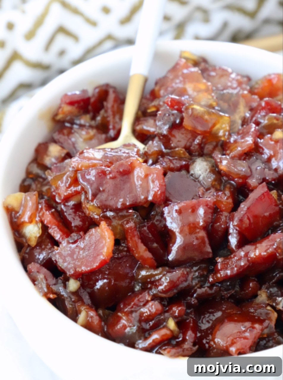 Sweet & Savory Bacon Preserve 14 Close-up of a bowl of homemade bacon jam, glistening and chunky, with a spoon ready to scoop. Perfect for sweet and savory dishes.
