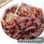 A bowl of delicious, glistening bacon jam with a spoon resting in it, ready to be served or enjoyed. Perfect for a savory and sweet treat.