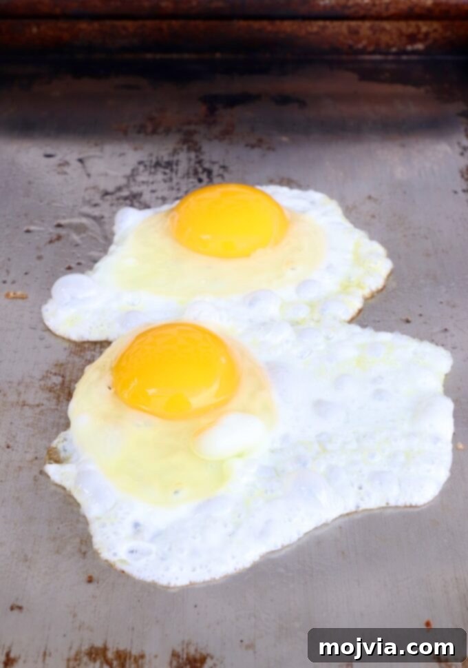 Sunrise Burger 7 Four eggs frying on a flat top griddle, with whites setting and yolks remaining perfectly runny.