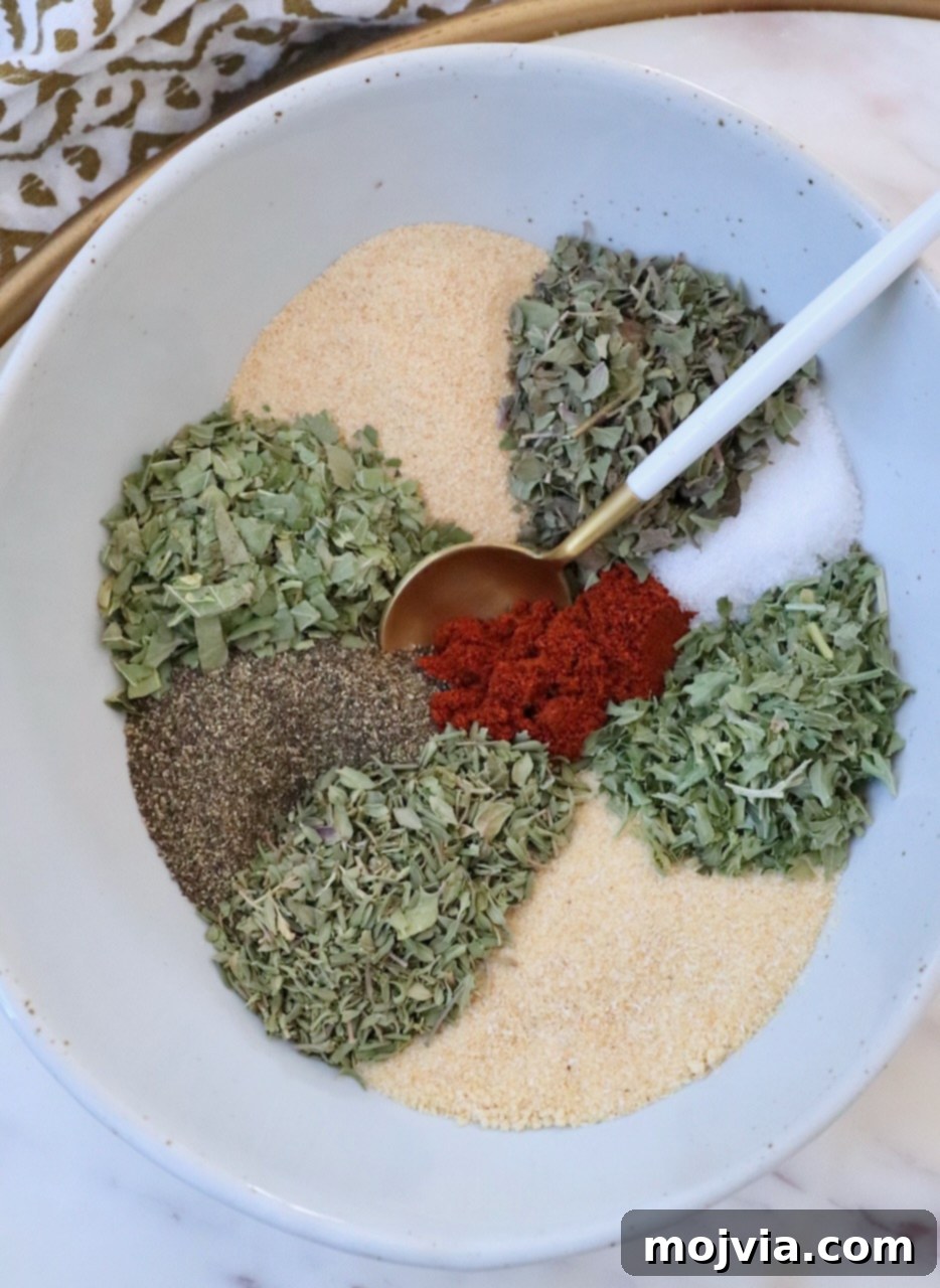 A selection of dried herbs and spices, separated in a bowl with a spoon, ready to be mixed for vegetable seasoning.