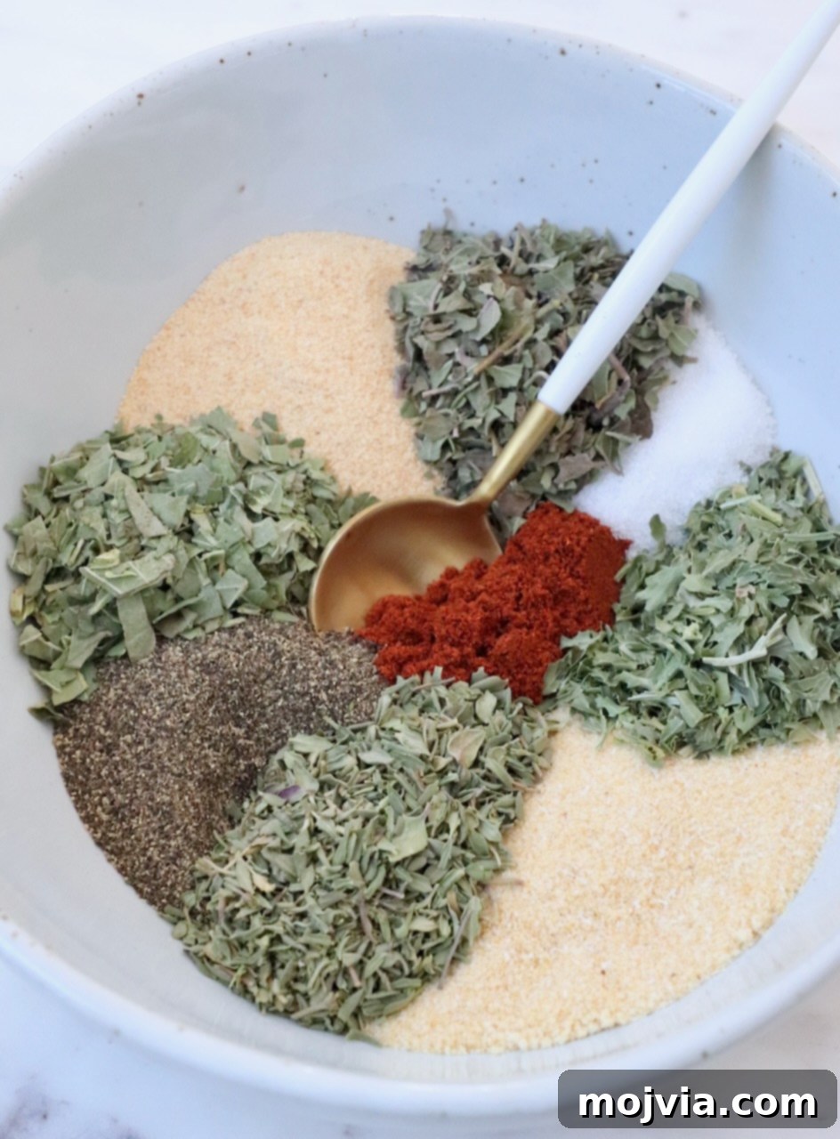 Assorted dried herbs and spices arranged in separate sections of a bowl with a spoon, showcasing the ingredients for homemade vegetable seasoning.