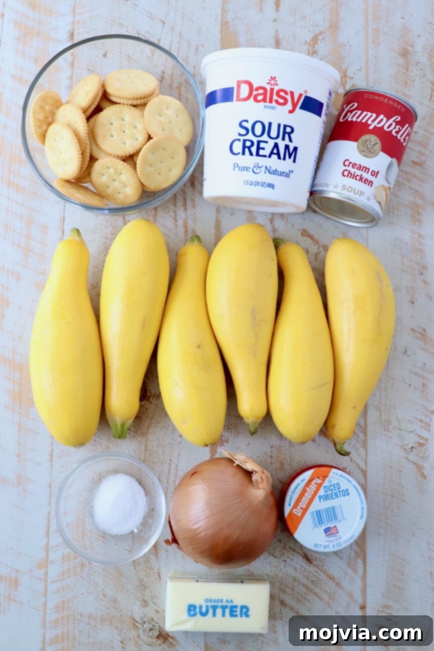 Golden Cheesy Squash Bake 3 A selection of fresh ingredients for making squash casserole, including yellow squash, onions, butter, sour cream, pimentos, and Ritz crackers, artfully arranged on a white wooden board.