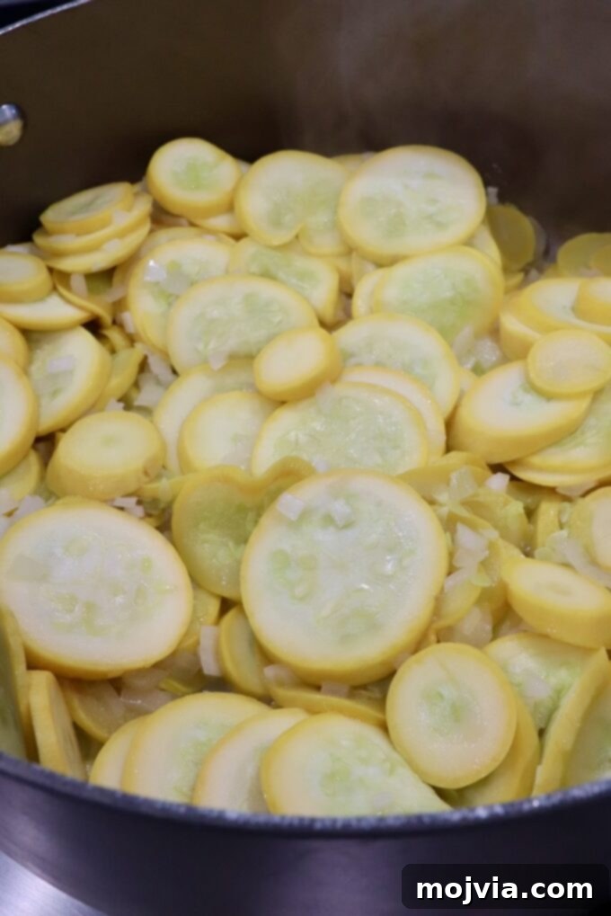 Golden Cheesy Squash Bake 5 Yellow squash and onions cooking down in a skillet, becoming tender and releasing moisture.