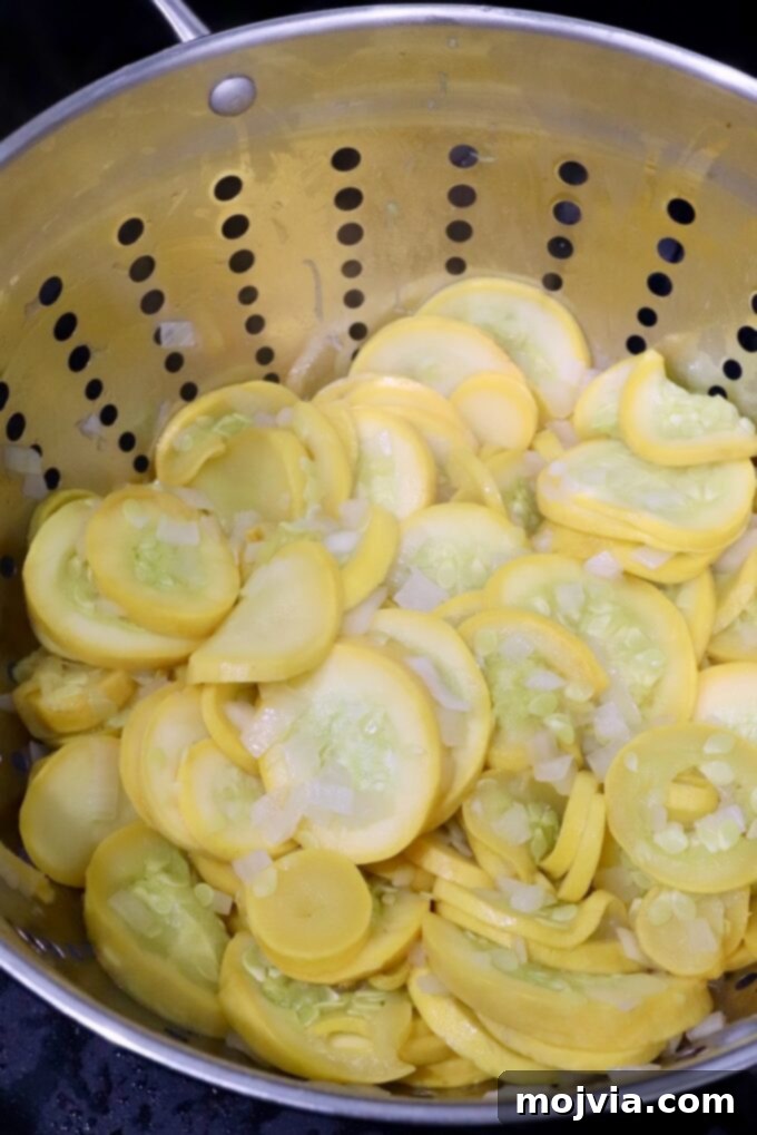 Golden Cheesy Squash Bake 6 Cooked squash and onions being transferred from the skillet into a colander for draining.