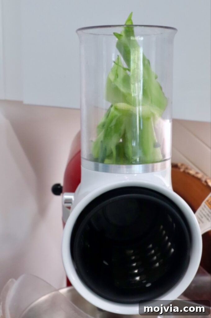 Vibrant Broccoli Slaw 5 Broccoli stems being shredded using an attachment on a KitchenAid stand mixer for efficient preparation.