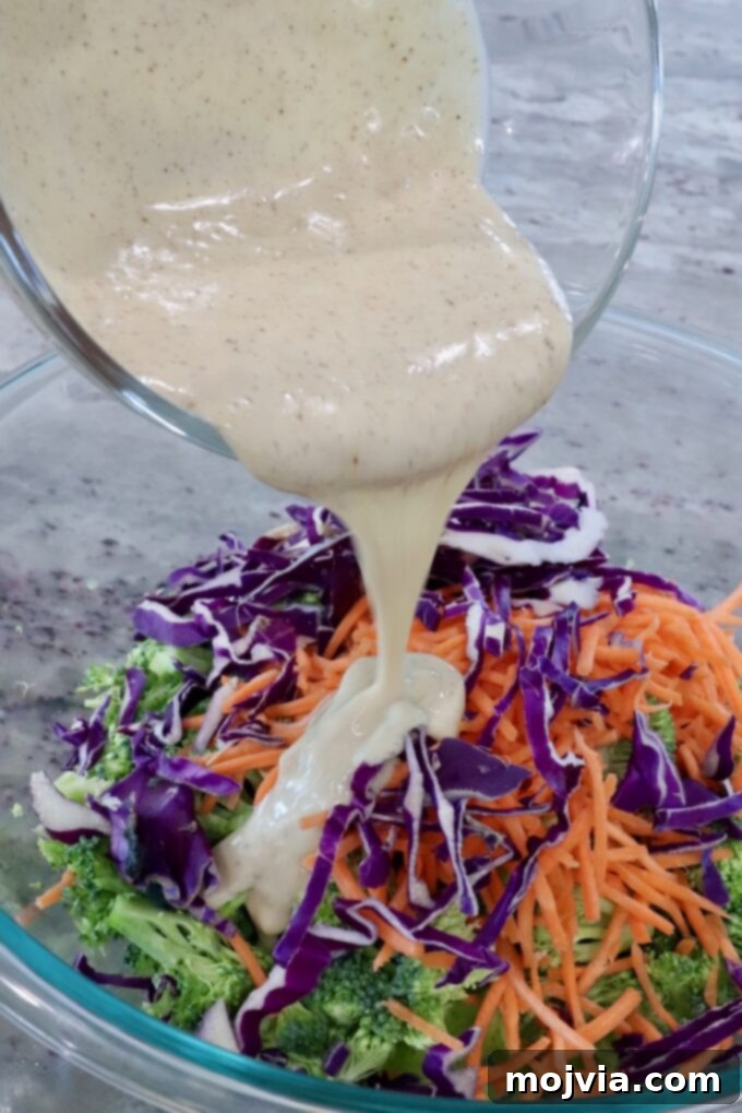 Vibrant Broccoli Slaw 9 Broccoli Slaw in a bowl with creamy dressing being poured over the vegetables, preparing for mixing.