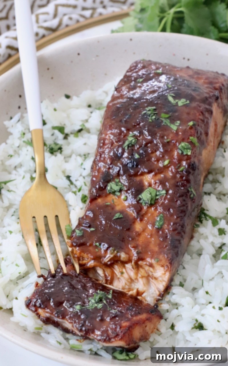 cooked glazed piece of salmon on top of rice in bowl with fork