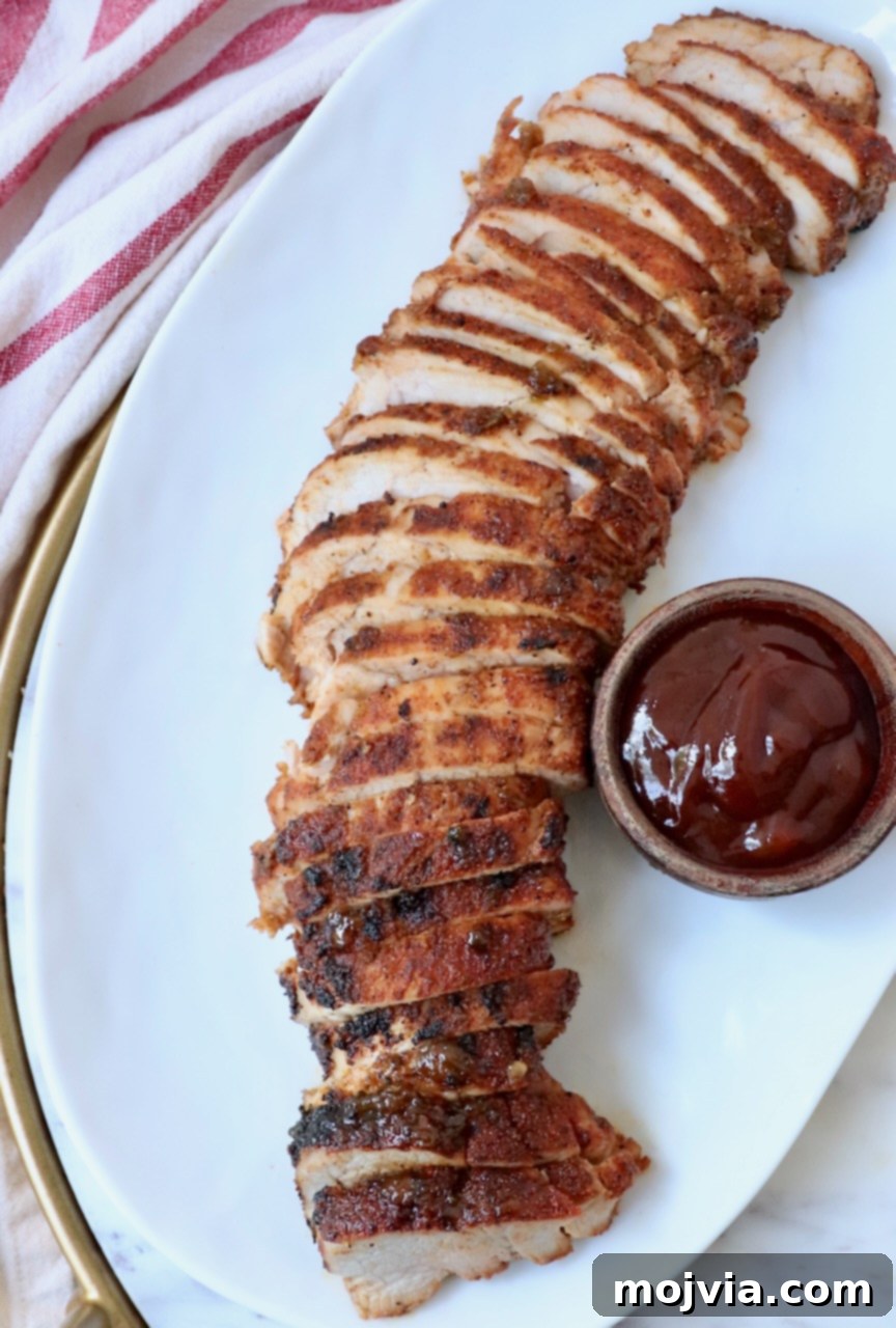 Fire-Kissed Pork Tenderloin 2 Sliced grilled pork tenderloin arranged artfully on a plate, with a small bowl of savory BBQ sauce on the side.