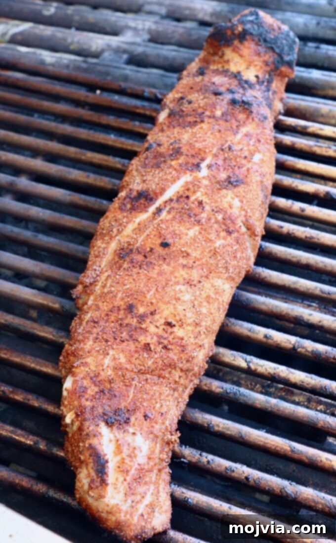 Fire-Kissed Pork Tenderloin 5 Seasoned pork tenderloin being seared on a hot grill, showing grill marks forming.