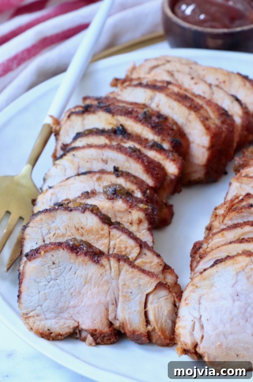 Fire-Kissed Pork Tenderloin 9 Appetizing slices of grilled pork tenderloin artfully arranged on a white plate, ready for serving.